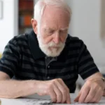 Elderly man working on a puzzle at a table.