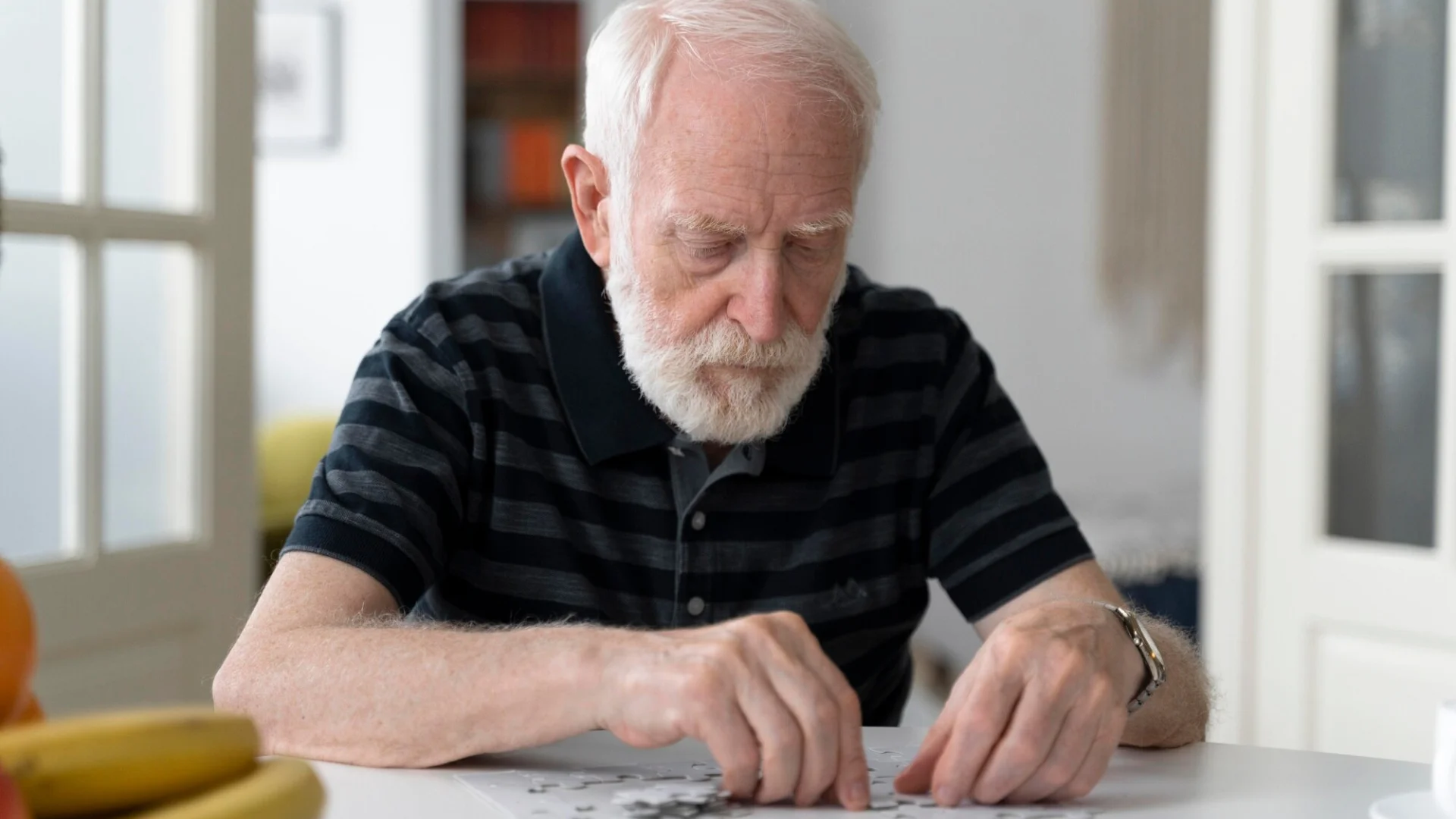 Elderly man working on a puzzle at a table.