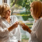 Two women sharing tea at home near a window.