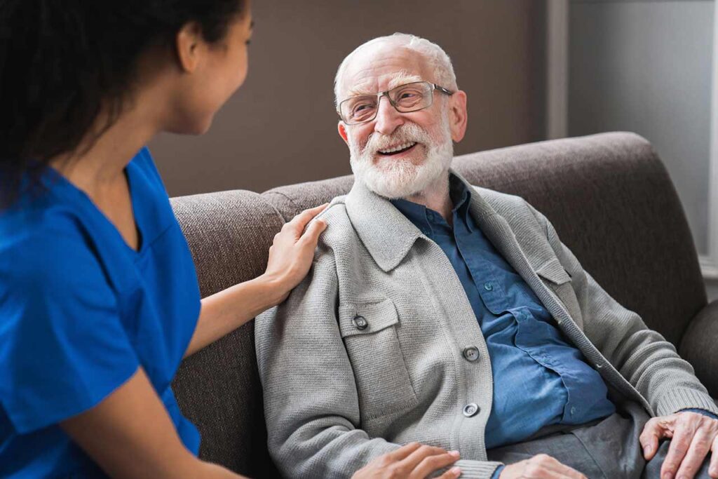 Caregiver listening sympathetically to seated elderly man.