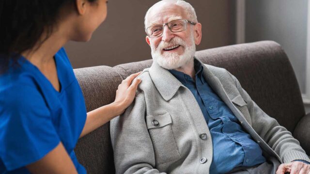 Caregiver listening sympathetically to seated elderly man.