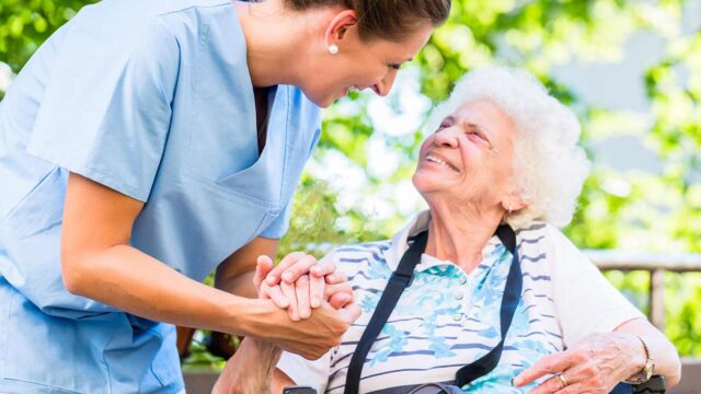 Nurse holding hands with elderly patient outside.
