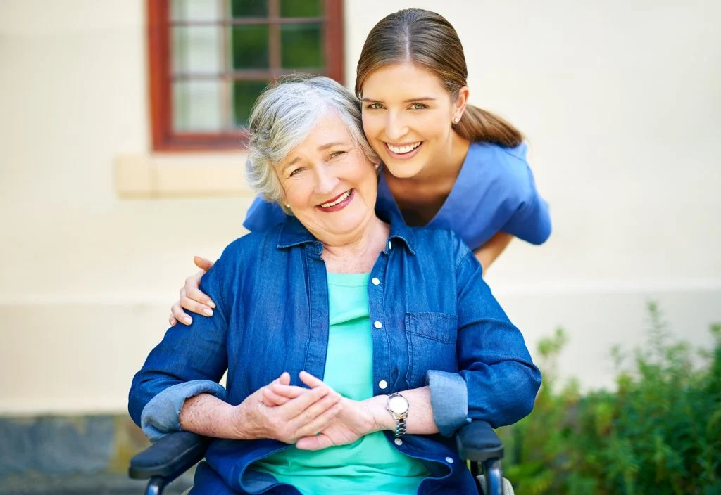 Young woman supporting senior in wheelchair outdoors.