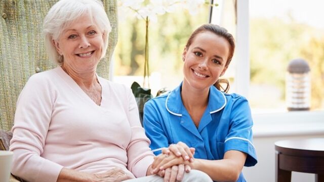 Caregiver and older woman holding hands on the sofa.