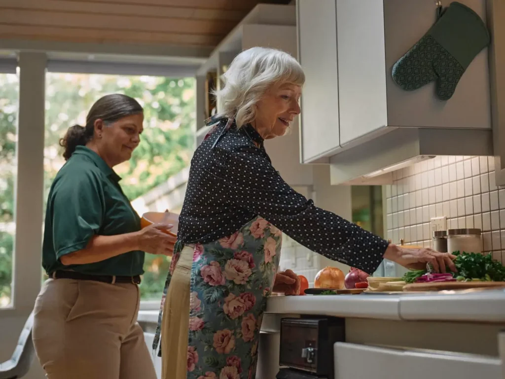 Home aide helping senior cook in kitchen.