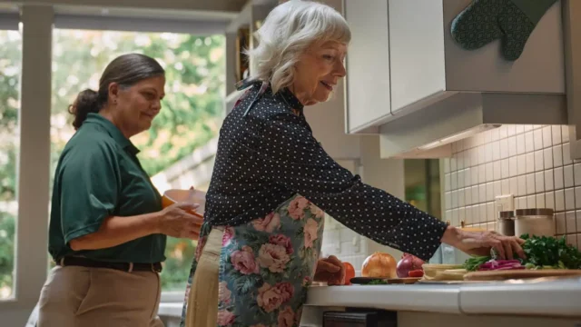 Home aide helping senior cook in kitchen.