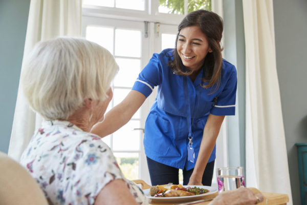 Care nurse serving dinner to a senior woman at home