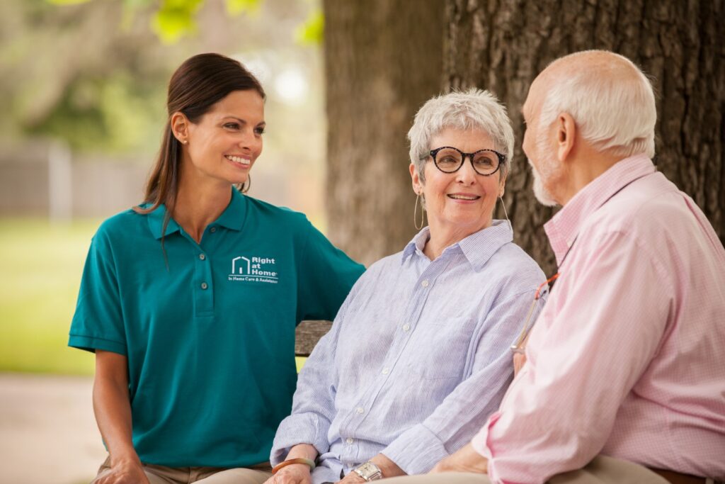 Caregiver assisting seniors seated outdoors.