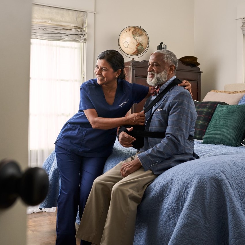 Physiotherapist guiding elderly man with arm stretch at home.