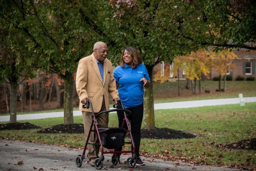 Elderly man using walker with companion in park.