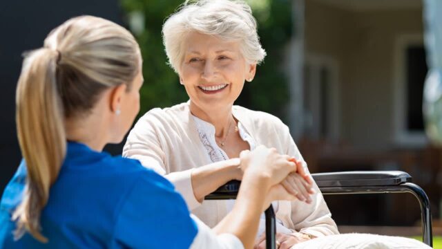 A doctor in blue scrubs attends to an elderly woman sitting in a wheelchair, ensuring her comfort.