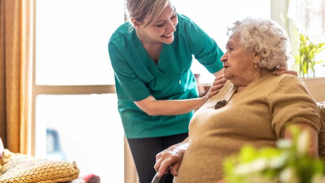 Nurse gently comforting elderly woman on sofa.