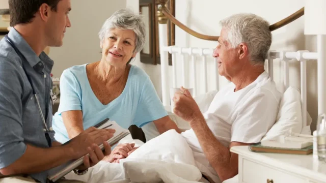 A caregiver and an elderly woman have a thoughtful conversation in a cozy room, both smiling.