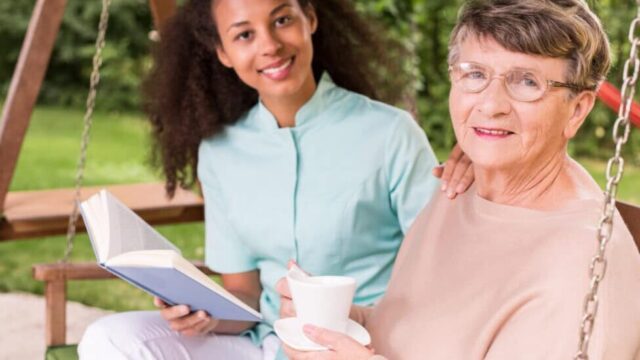 Friendly caregiver talking with elderly woman on a couch.