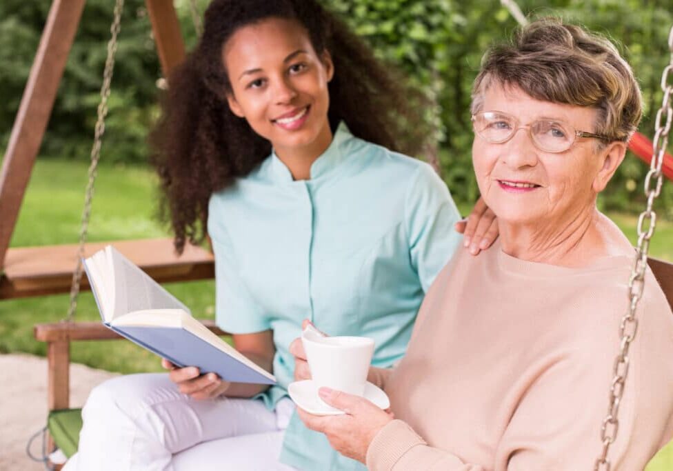 Friendly caregiver talking with elderly woman on a couch.