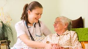A caregiver in scrubs and an elderly woman smile at each other while holding hands, sharing a warm and joyful moment.