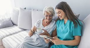 A caregiver and elderly woman enjoy a peaceful moment together, sipping tea and looking at a tablet, sharing a smile.