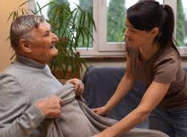 A caregiver helps an elderly man by arranging a blanket over him in a cozy room.