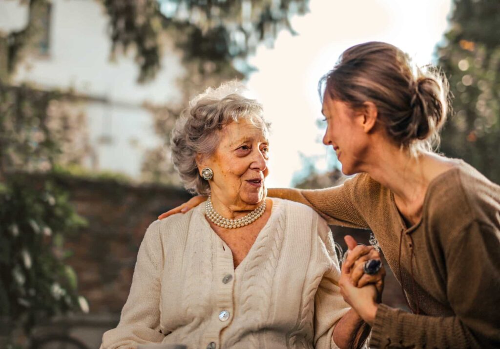 A healthcare professional helps an elderly woman in a wheelchair, offering emotional and physical support.