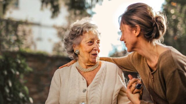 A healthcare professional helps an elderly woman in a wheelchair, offering emotional and physical support.