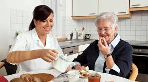 A caregiver joyfully serves breakfast, ensuring a moment of comfort and companionship for the elderly patient.