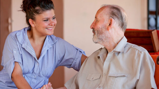 A caregiver and an old man having a thoughtful conversation in a cozy room, both smiling.